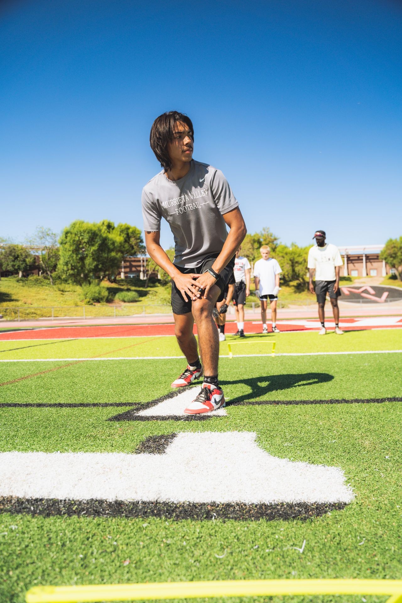 Athlete practicing football drills on field with teammates in the background.