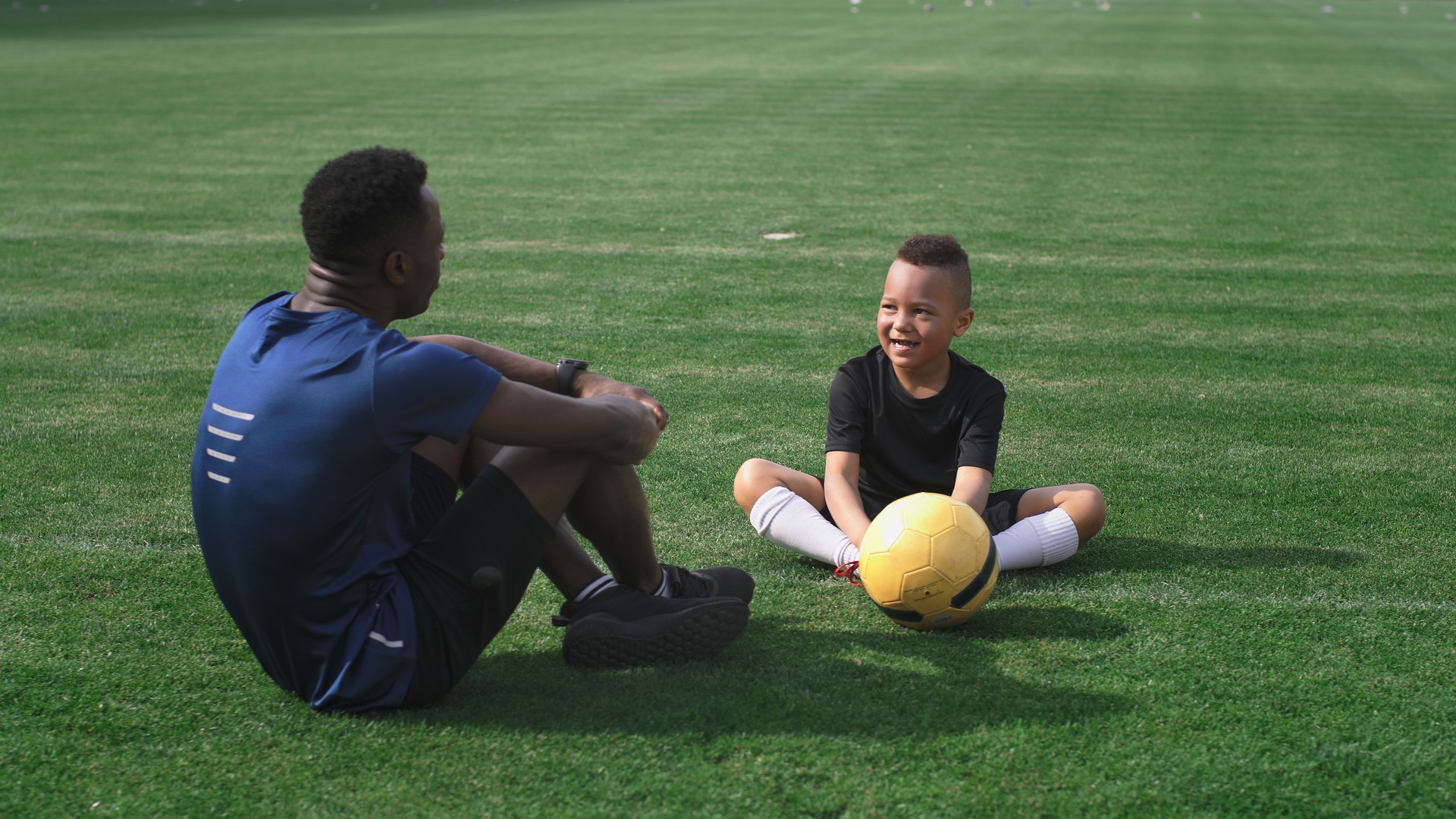 Diverse trainer and boy talking on football pitch