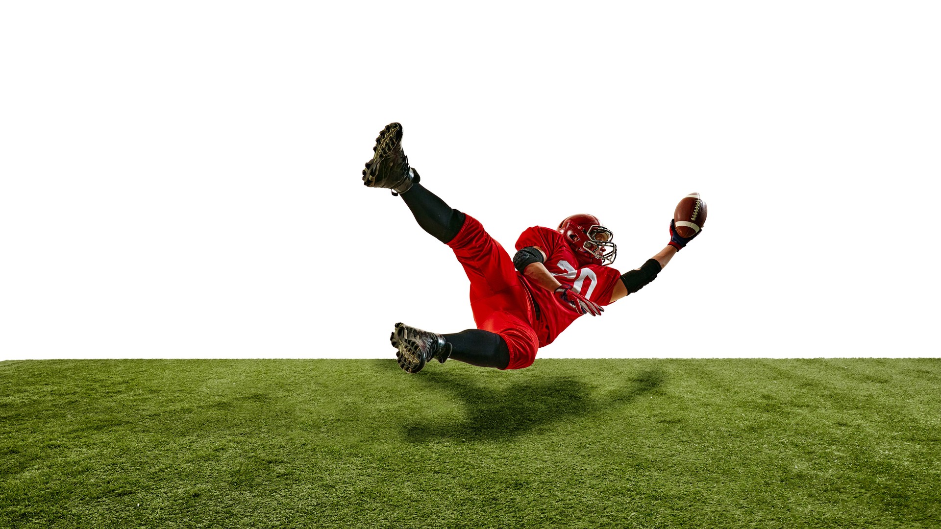Intense moment o American football player diving to catch ball, dressed in red uniform with helmet, isolated against white background.
